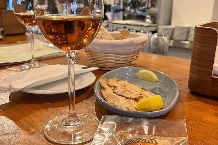 A table with a glass of wine, a plate with food, and a basket in the background. 4