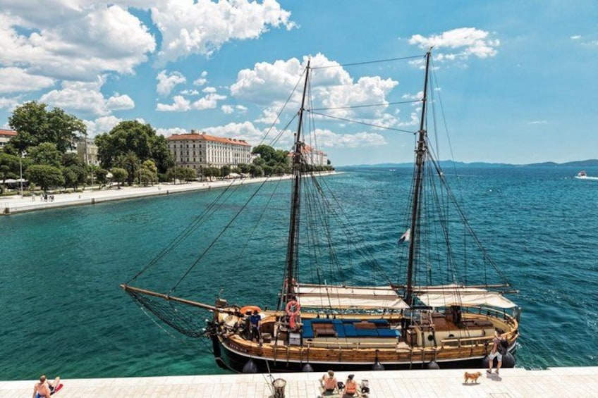 A sailing ship on a calm sea with a cityscape in the background. 2