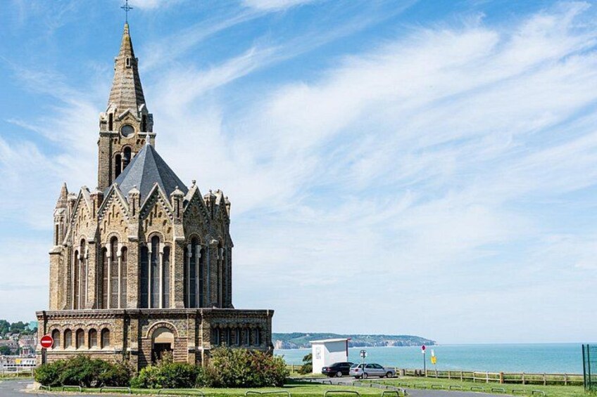 Eine gotische Kirche mit einem hohen Kirchturm, einem großen Bogenportal und Blick auf das Meer im Hintergrund. 2