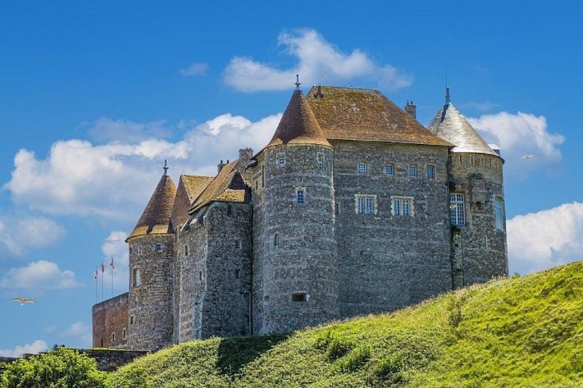 A historic stone castle with multiple towers and a grassy hill in the foreground. 2