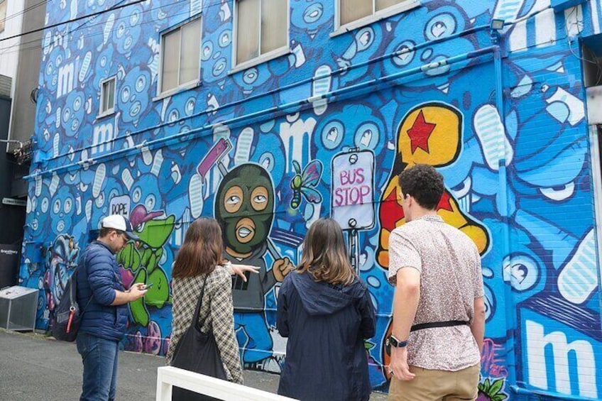 A mural with a bus stop sign and people observing it. 1