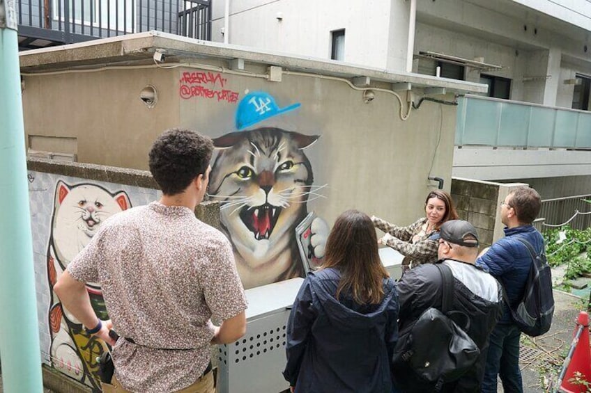 A group of people standing in front of a mural of a cat wearing a hat. 5