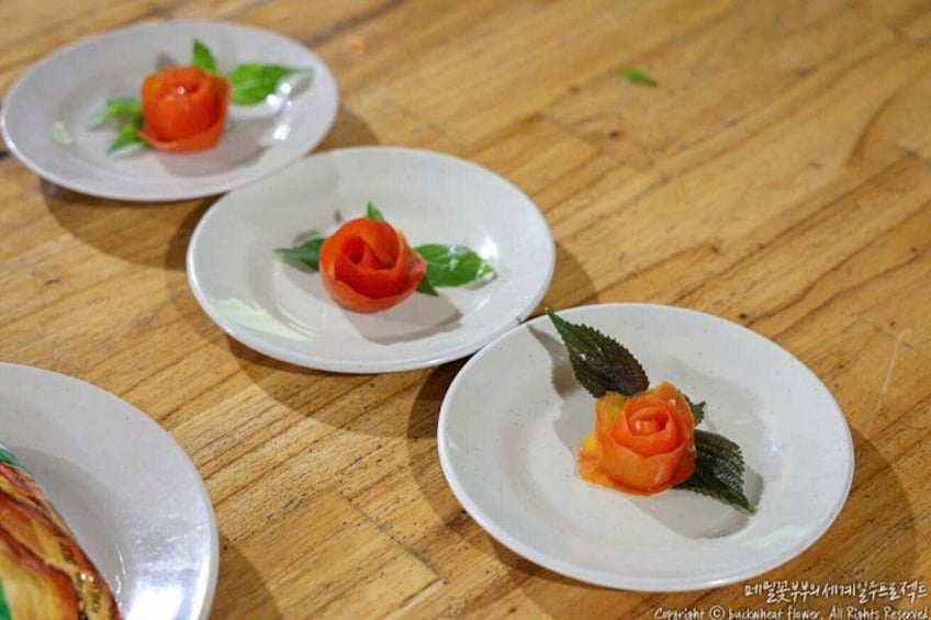 Three white plates with rose-shaped food items on a wooden table. 4