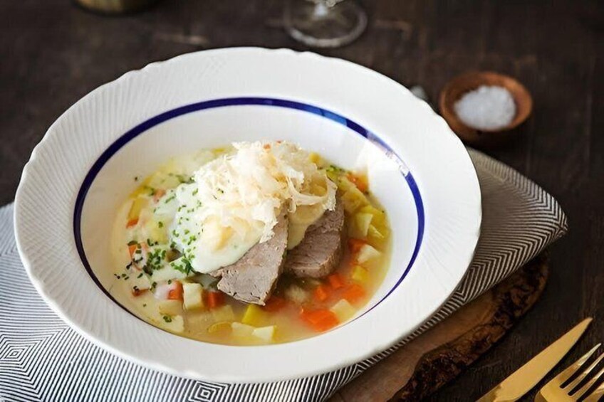 A bowl of soup with meat, vegetables, and a topping. 3