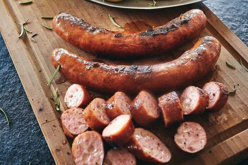 Two grilled sausages and sliced sausage pieces on a wooden board. 5