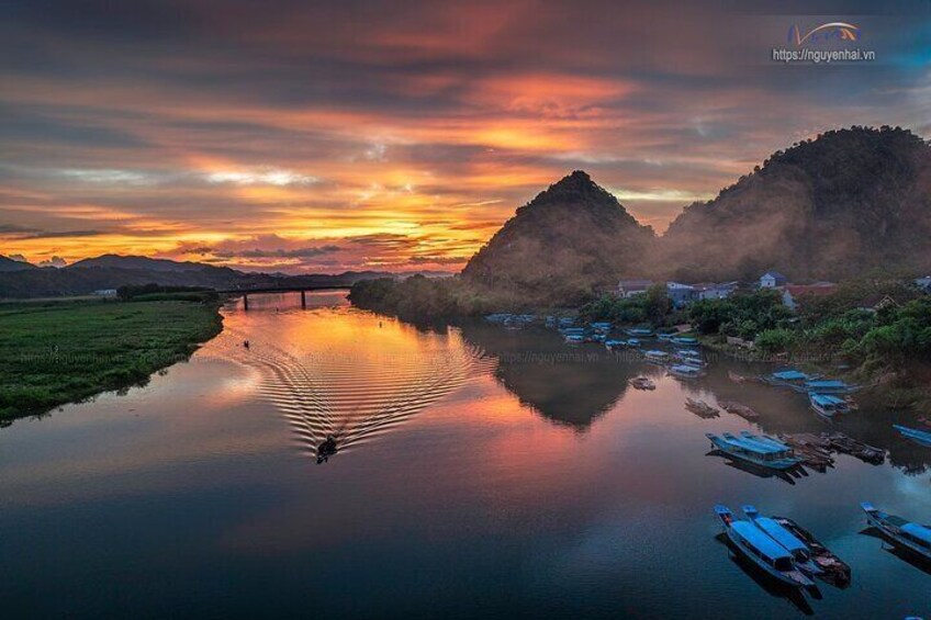 A calm river reflecting the sunset, boats, and a bridge. 1