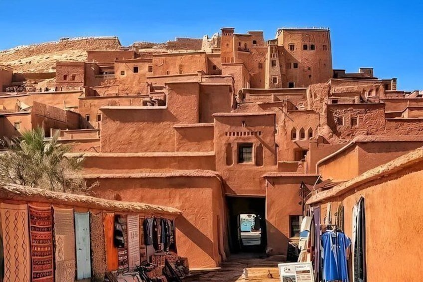 A traditional Moroccan town with terracotta buildings, narrow alleys, and a prominent fortress-like structure in the background. 3