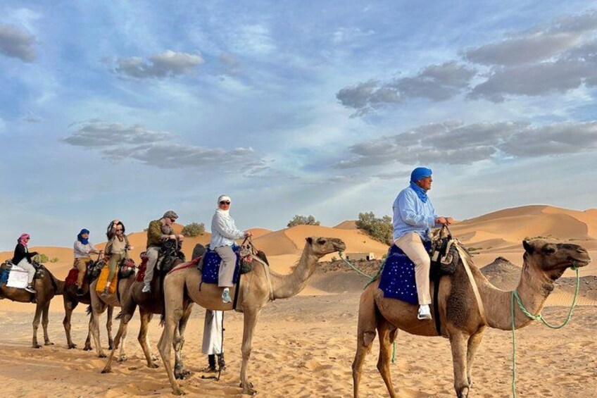 A group of people riding camels in a desert landscape with sand dunes in the background. 1