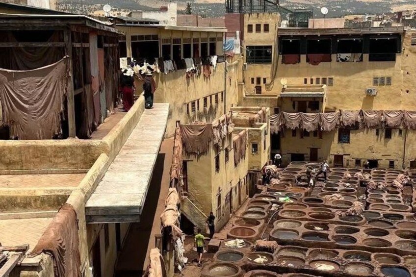 A traditional Moroccan courtyard with terracotta pots, a staircase, and people walking. 5