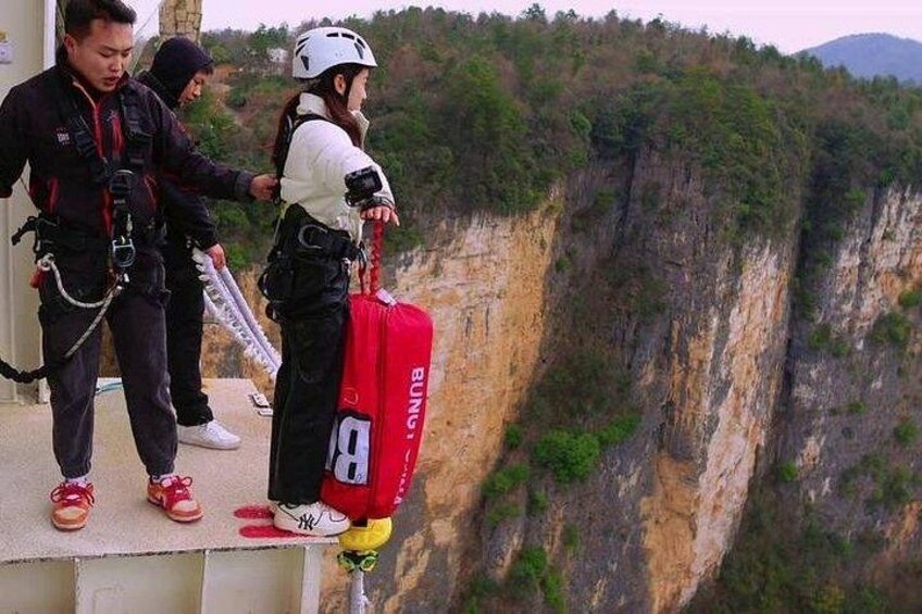 Una persona con casco blanco y mochila roja de pie en un saliente con vista a un acantilado. 2