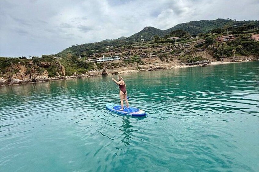 A person on a blue paddleboard in a body of water with a hilly landscape in the background. 3