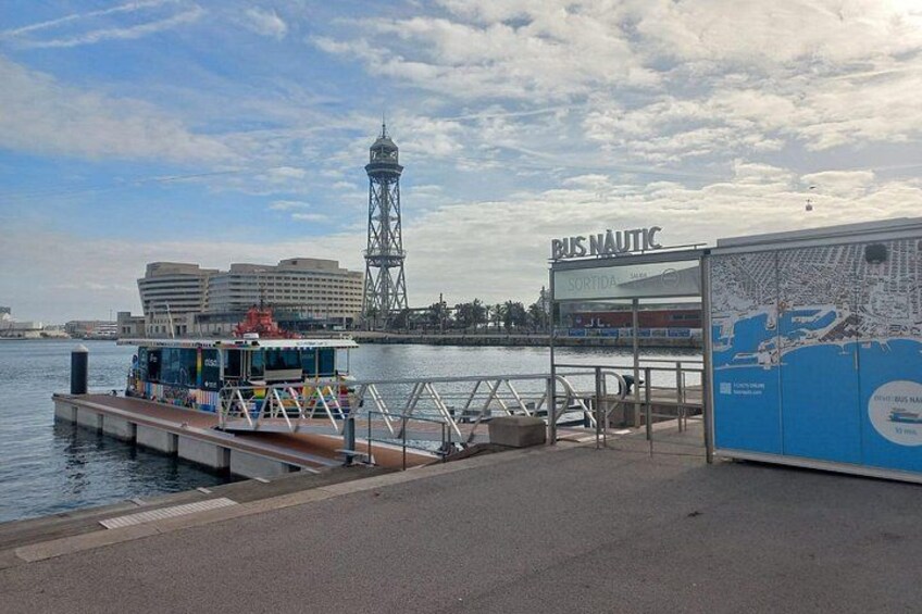 Een waterkant met een veerterminal, een steiger en een hoge toren op de achtergrond. 1