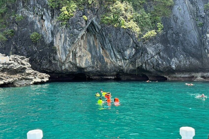 Un grupo de personas nadando en un mar turquesa con acantilados rocosos al fondo. 3