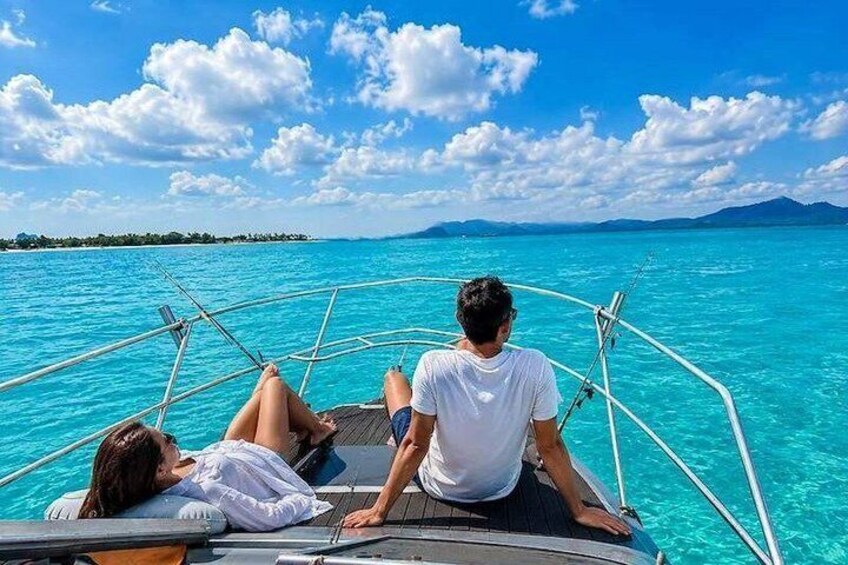 Un bote con dos personas sobre un mar turquesa, cielo despejado y tierra a lo lejos. 1