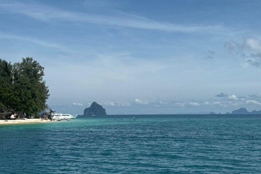Una playa con agua turquesa cristalina, una pequeña isla y una cadena montañosa distante. 2