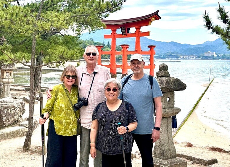 A group of people standing in front of a red torii gate with a body of water and mountains in the background. 5
