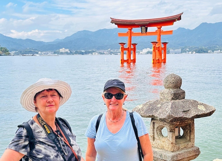Two people standing by a stone lantern and a red torii gate with mountains in the background. 2