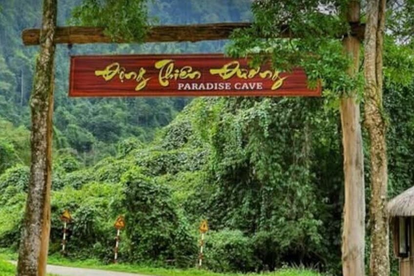 A wooden sign with 'Dirt Bike Paradise Cave' written on it, set against a lush green forest backdrop. 1