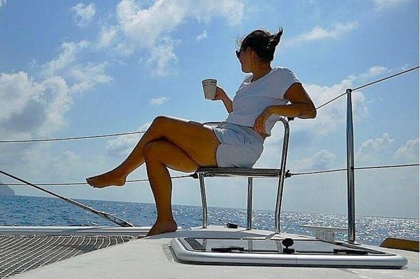 A person sitting on a boat with a drink, wearing a white shirt, and the ocean in the background. 5