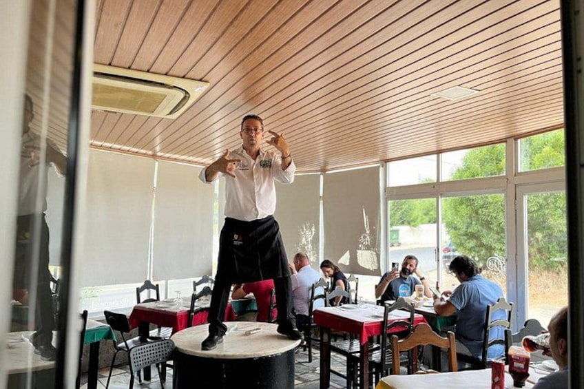 Eine Person steht auf einem Hocker in einem Restaurant mit Tischen und Stühlen, durch große Fenster ist die Außenwelt sichtbar. 2
