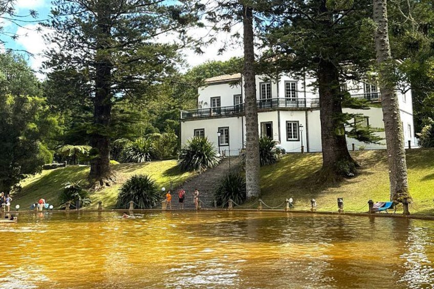 A white building with a balcony, surrounded by trees and a body of water. 4