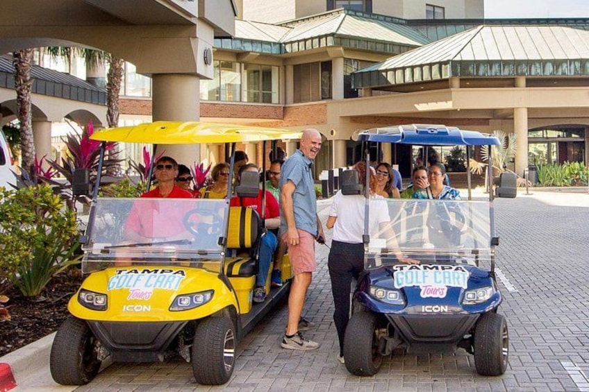 Dos carritos de golf estacionados frente a un edificio con palmeras y un sendero pavimentado. 4