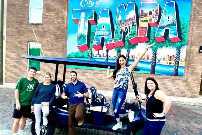 A group of people posing in front of a mural with the text 'City of Tampa.' 2