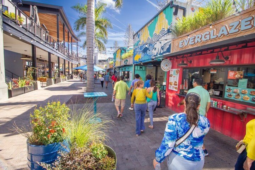 A bustling street with people walking, a restaurant named 'Everglaze', and a blue planter with plants. 5