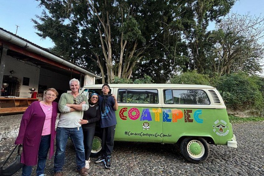 A green van with colorful lettering and a logo, parked in front of a building with trees in the background. 1
