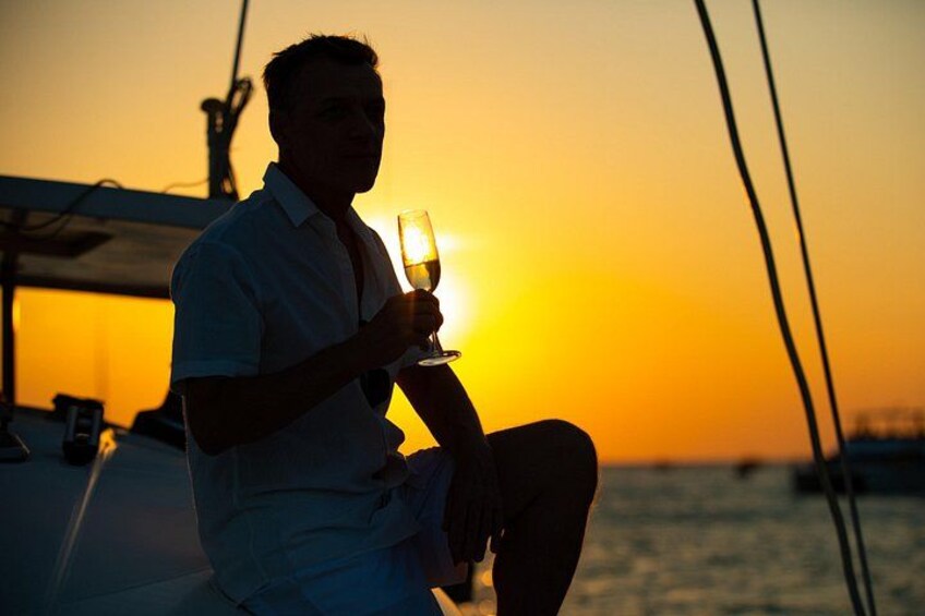A person sitting on a boat holding a glass of wine, with the sun setting in the background. 3