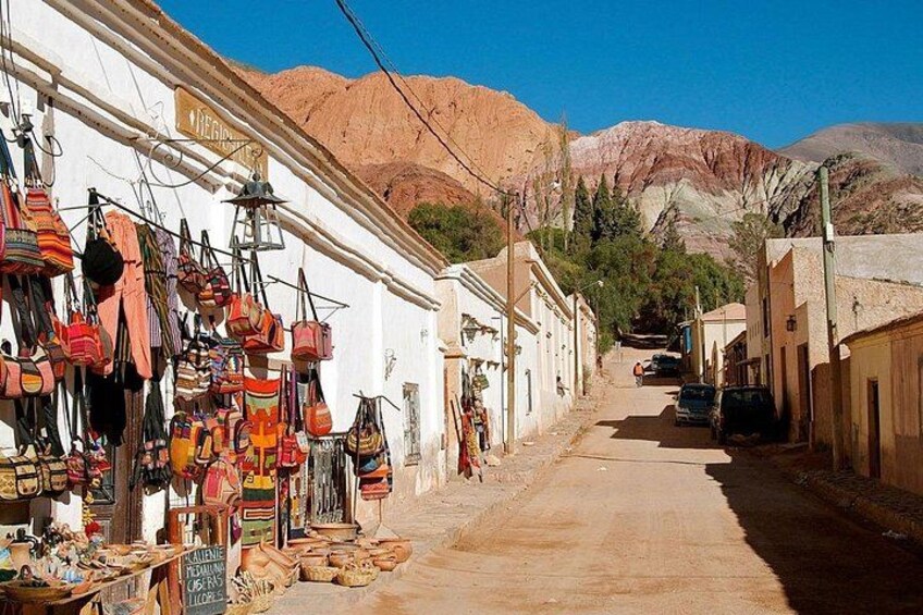 A narrow street with shops on one side and a mountain in the background. 1