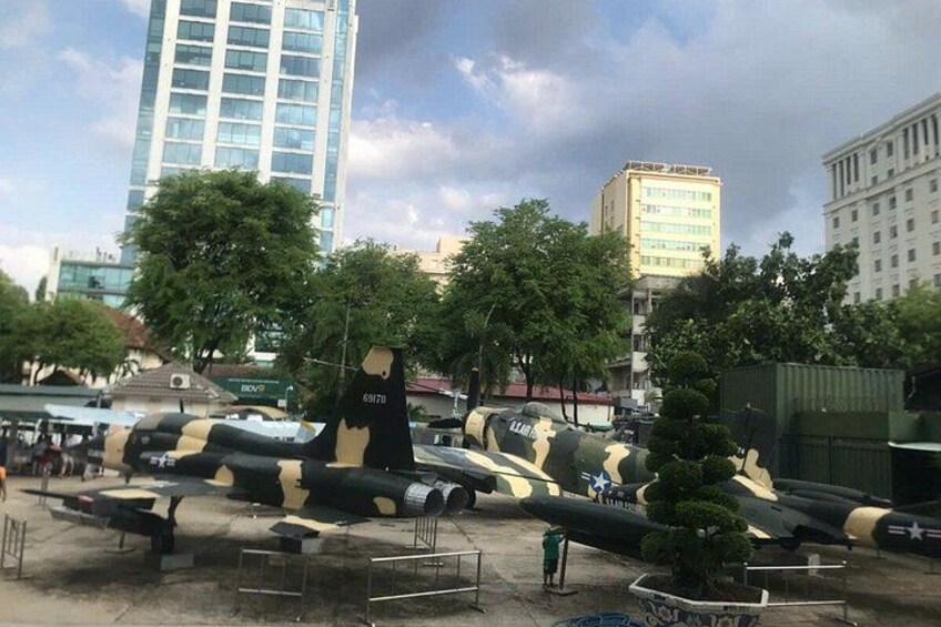 A military aircraft on display with camouflage paint, surrounded by trees and buildings in an urban setting. 3