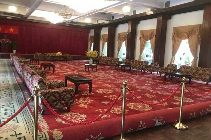 A formal room with a red carpet, rows of chairs, and a long table. 5