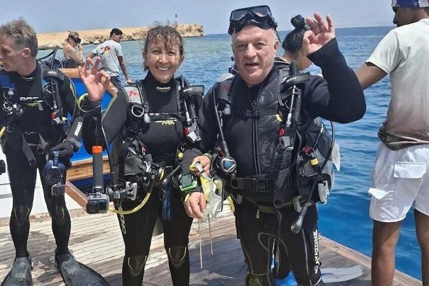 Dos buzos con equipo completo de buceo en un muelle de madera junto al mar. 2
