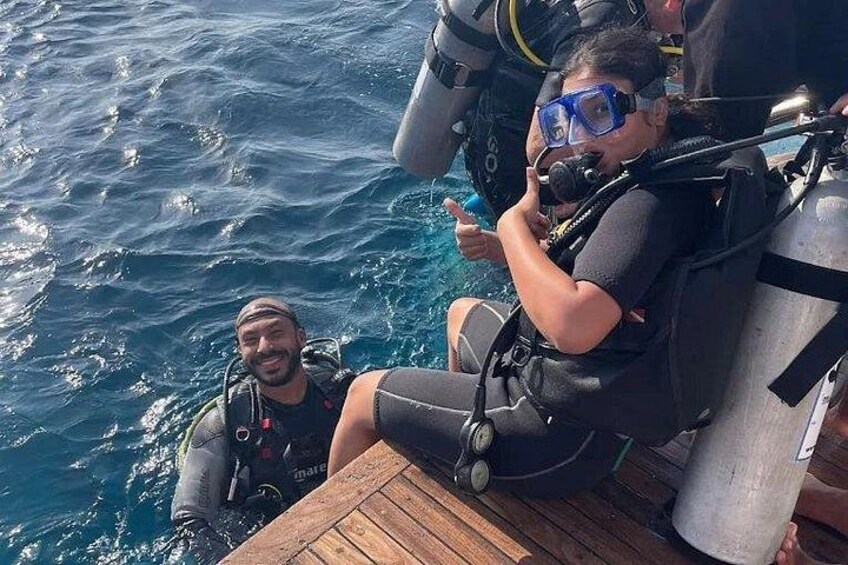 Dos personas con equipo de buceo en un bote, con el océano al fondo. 5