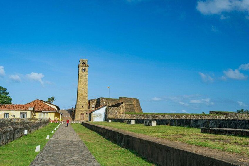 A historical fort with a tall tower, a paved pathway, and surrounding grassy areas. 2