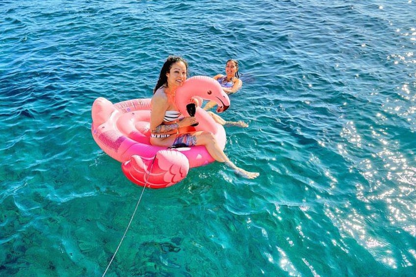 Two people floating on a pink inflatable raft in clear blue water. 4