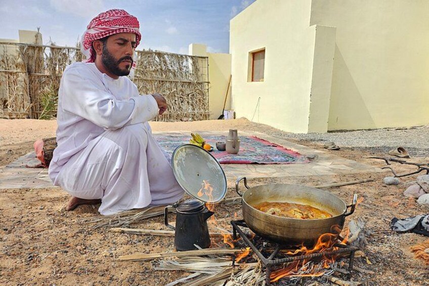 A person cooking outdoors with a pot on a stove, surrounded by a rural setting. 3