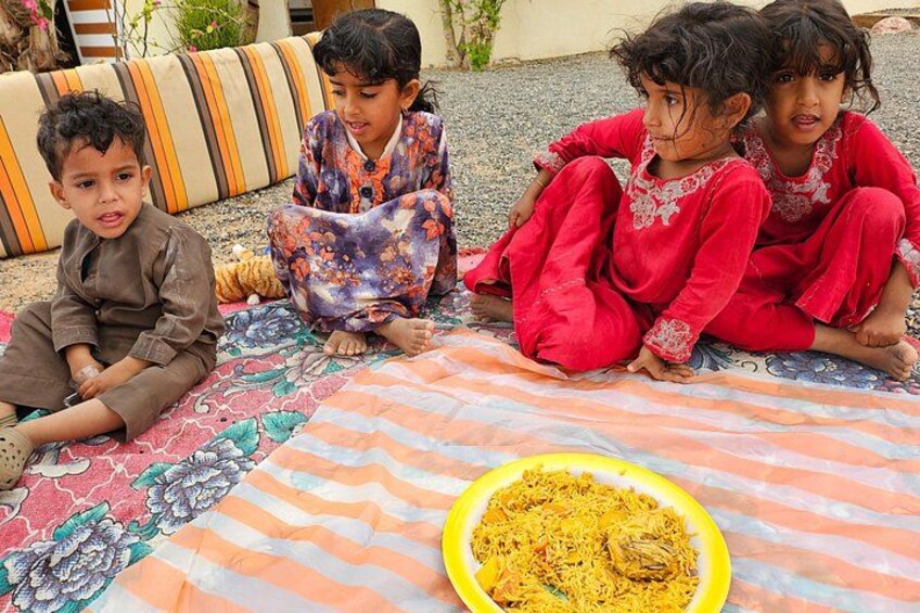 Children sitting on a patterned rug with a bowl of food in the foreground. 2