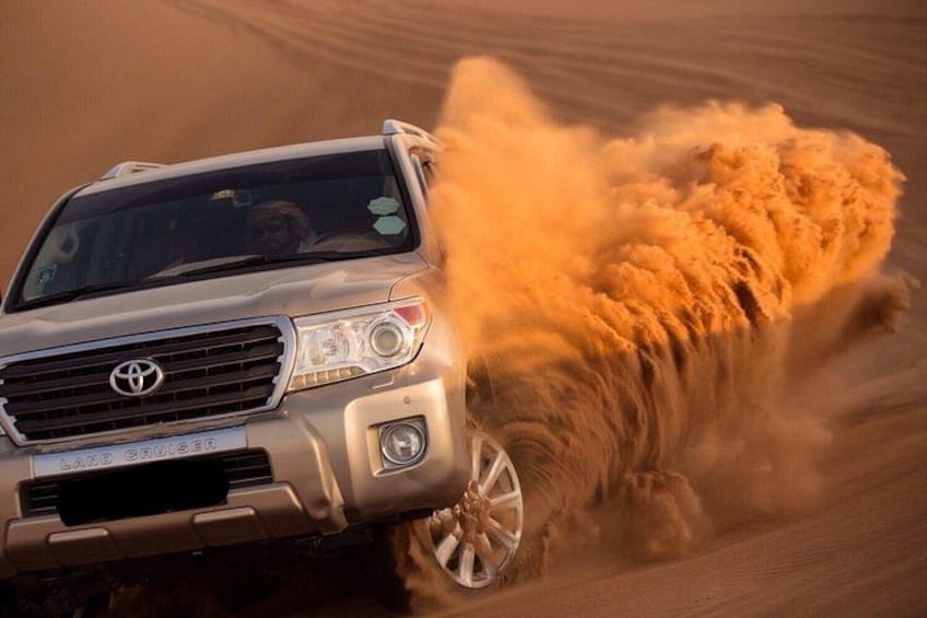 A vehicle driving through a sandy terrain, kicking up dust. 1