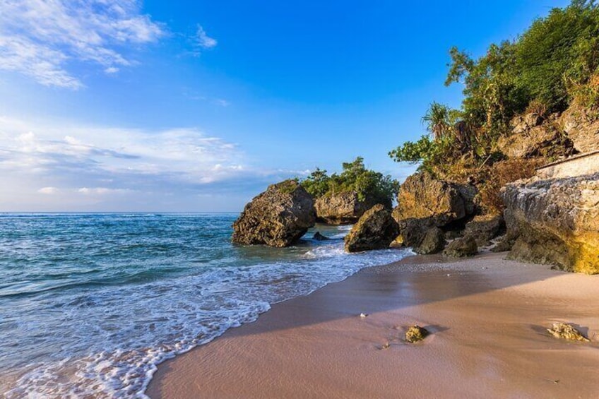 A beach with clear blue water, sandy shore, and rocky outcrops with vegetation. 5