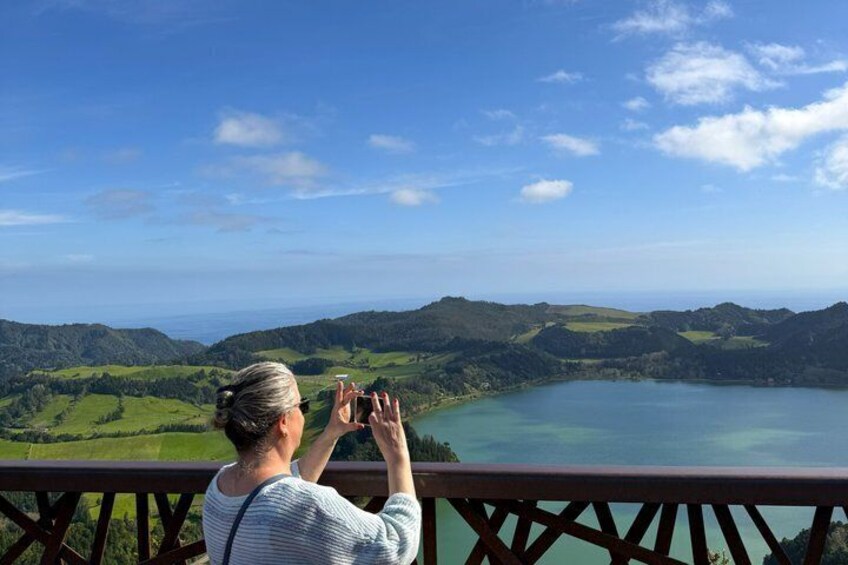 A person taking a photo of a lake surrounded by green hills. 3