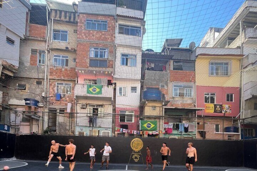 Eine Gruppe von Menschen spielt auf einem Außen-Tennisplatz, umgeben von bunten Gebäuden. 1