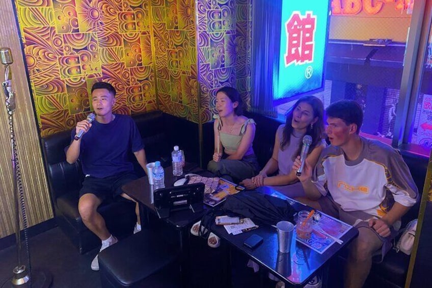 Four people sitting on a couch in a room with colorful wall patterns and a neon sign. 2