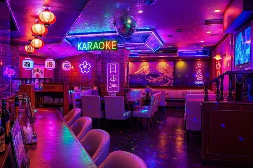 A karaoke bar with neon signs, Japanese decor, and a stage. 4