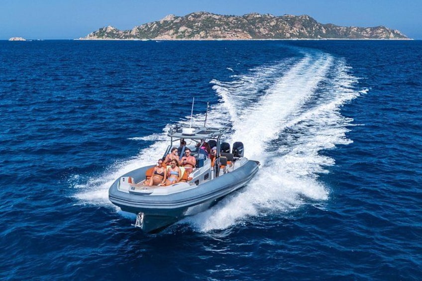 A motorboat with passengers on a clear day, moving through blue water with a wake behind it, and a rocky island in the distance. 2