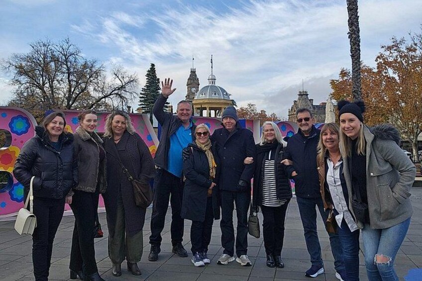 A group of people standing in a public square with a colorful mural and a historic building in the background. 5