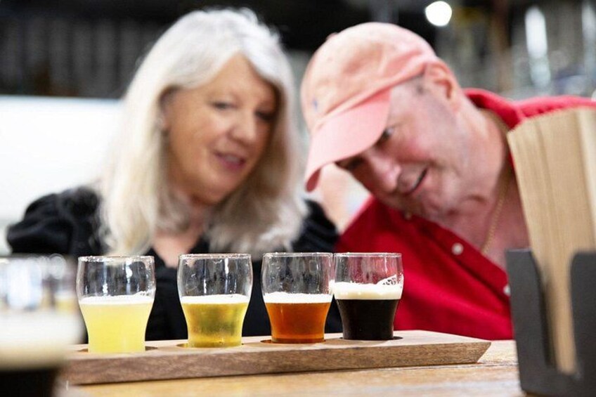 A person in a red shirt and a cap, seated at a table with four glasses of different colored beverages. 2