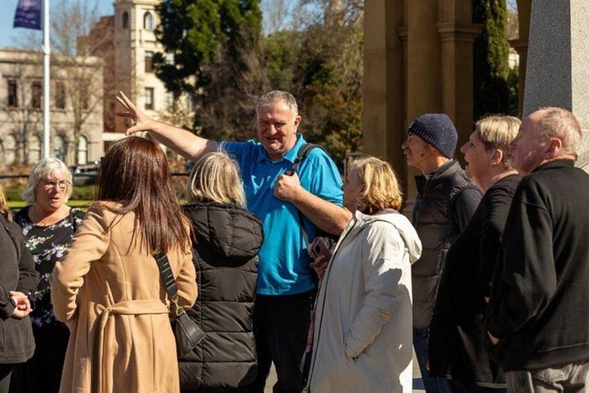 A group of people gathered outdoors, some standing and others sitting, with a building and trees in the background. 3