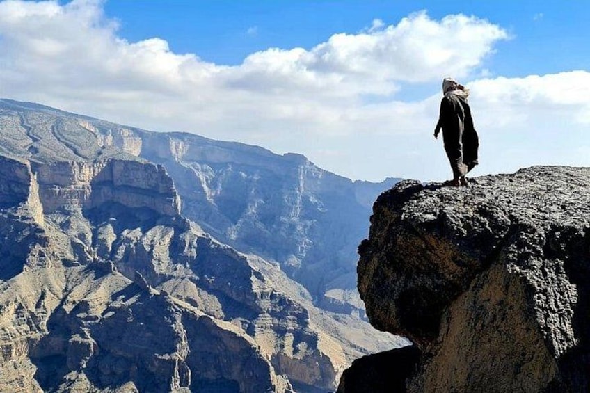 A person standing on a rocky cliff overlooking a vast canyon with layered rock formations. 1
